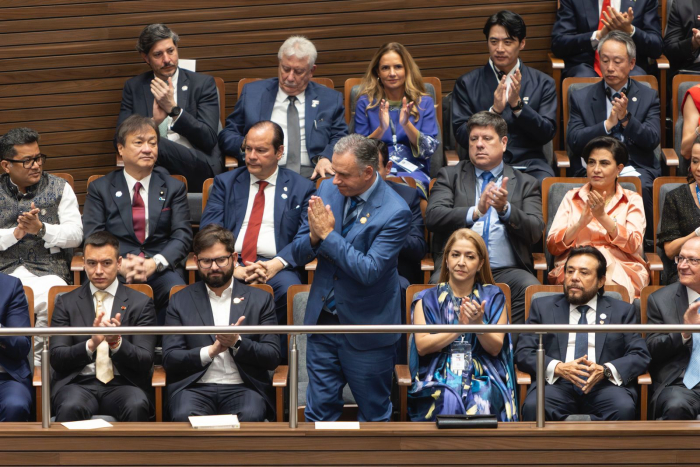 Líderes y diplomáticos internacionales aplauden en un auditorio mientras Orsi saluda de pie en el ce