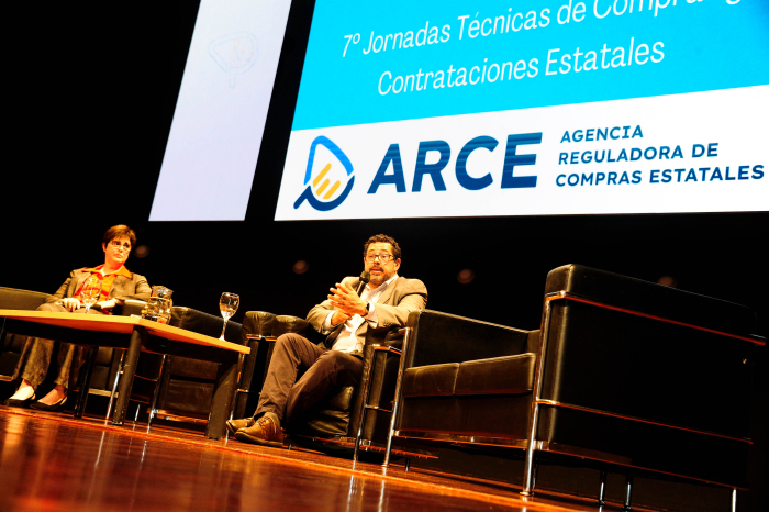 El secretario de Presidencia diserta sentado, con micrófono en mano, sobre un escenario.