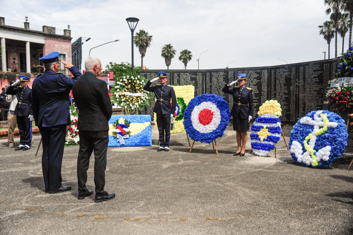 Ministro del Interior y varios militares saludan, frente a una pared conmemorativa