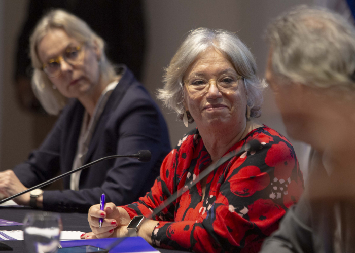 Directora de Inmujeres sentada en mesa con micrófono mira hacia un costado sonriendo 