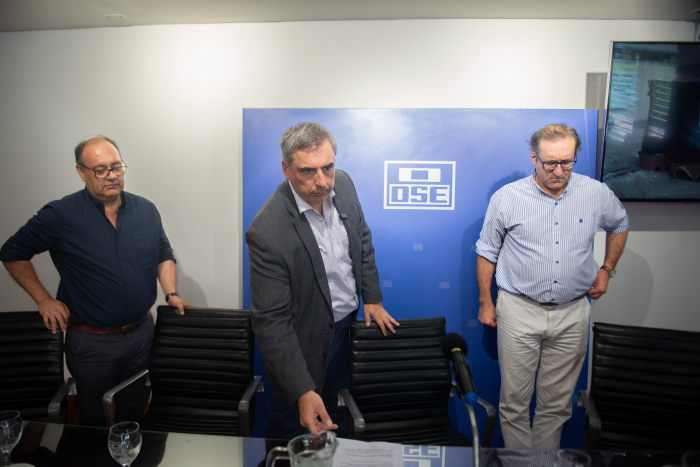 Presidente de OSE, de pie, junto a dos oradores se preparan para disertar