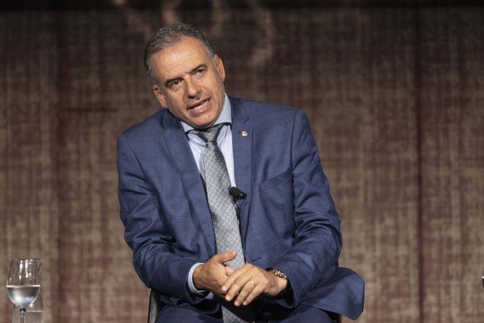 Orsi, de perfil, sentado en un sillón en el escenario diserta