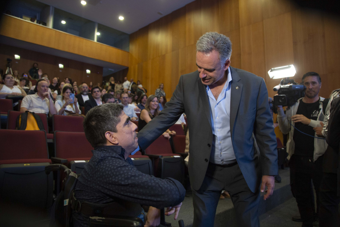 Orsi saluda a un usuario en silla de ruedas en la platea del auditorio de la Torre Ejecutiva. 