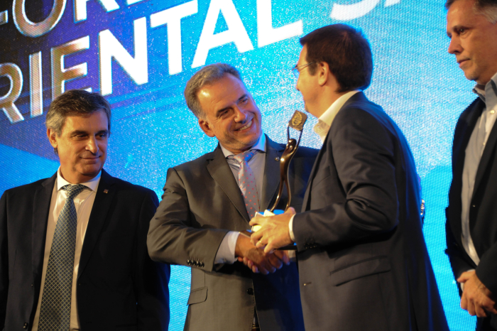 Orsi le estrecha la mano y le entrega una estatuilla a un empresario en el escenario.