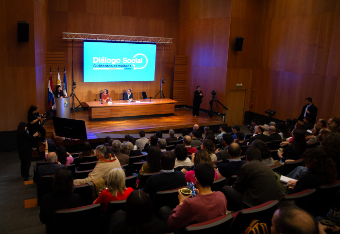 Sala del evento vista desde atrás con público y expositores
