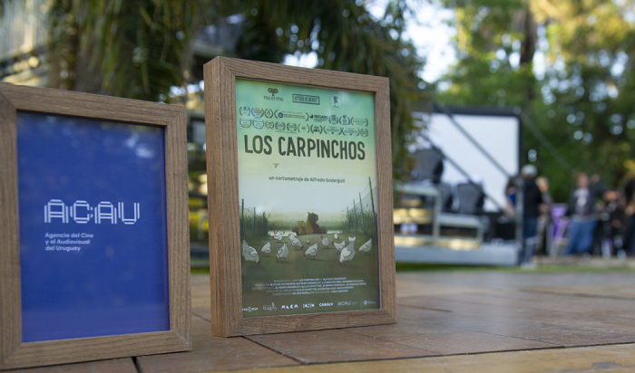 Cuadros ubicados en una mesa, en el jardín de la Residencia Presidencial. En uno de ellos, el logo de ACAU; en el otro, el afiche del cortometraje "Los carpinchos"