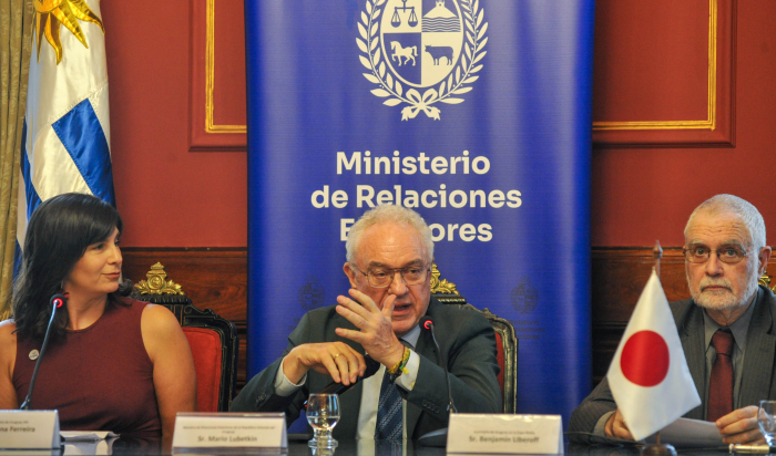 Canciller Mario Lubetkin habla en una mesa. A su lado, el comisario en Expo Osaka 2025 y la directora de Uruguay XXI. Frente a ellos, una bandera de Japón