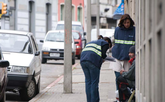 Dos funcionarias del Ministerio de Desarrollo Social, de pie, dialogan con una persona sentada en la vereda