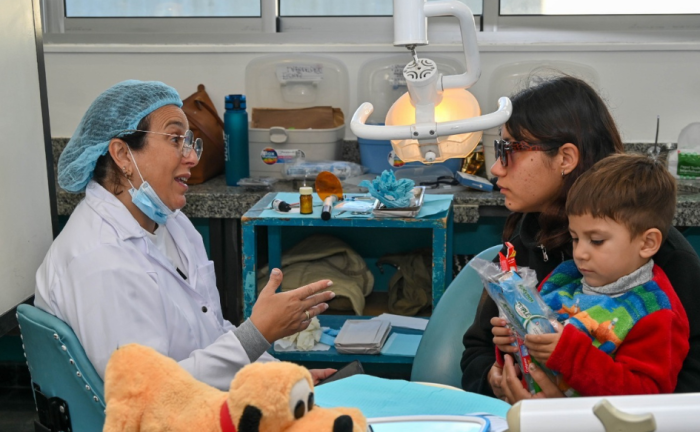 Plan Juntos superó los 4.000 tratamientos odontológicos en 2025 Odontóloga habla con una paciente, que tiene un niño de unos cinco años sentado en su falda, en un consultorio odontológico