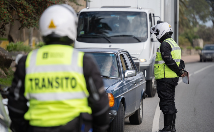 Uruguay busca junto a 21 países iberoamericanos reducir un 50% la siniestralidad vial hacia el 2030 Un inspector de tránsito, de pie, dialoga con el chofer de una auto detenido en la vía pública. Delante de ellos, otro inspector los observa. En su chaleco dice "tránsito".