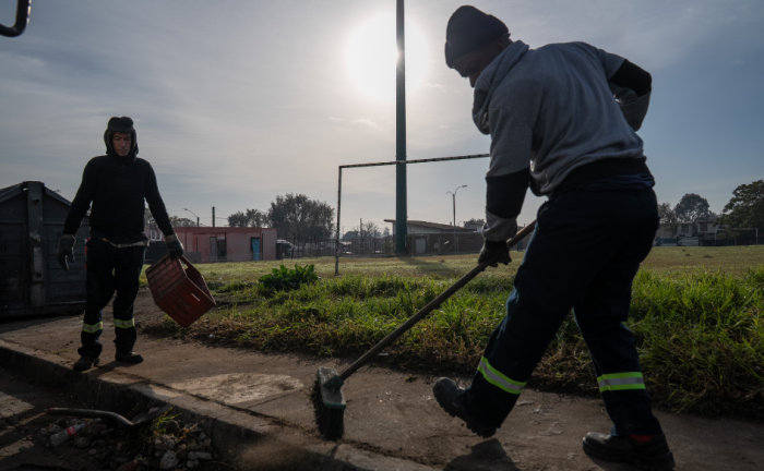 Dos funcionarios que trabajan para la Intendencia de Montevideo barren una vereda en Cerro Norte