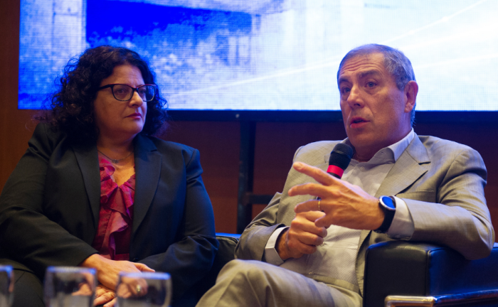 Ministro de Economía y Finanzas, Gabriel Oddone, habla sentado en un sillón, con un micrófono de mano. A su lado, la contadora general de la Nación, Adriana Arosteguiberry