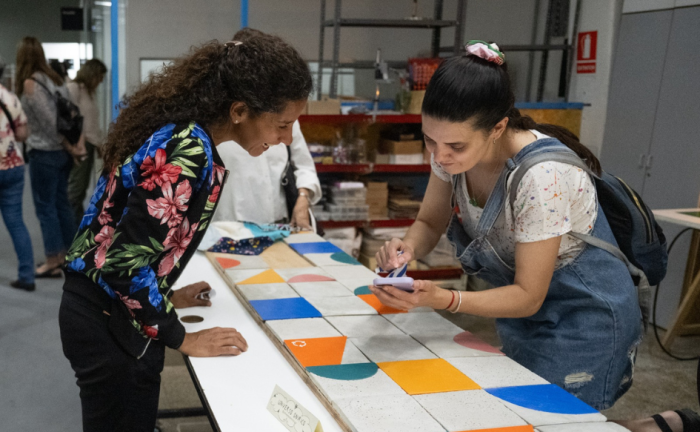 Una mujer sostiene un celular y se lo muestra a otra en un taller de artesanías