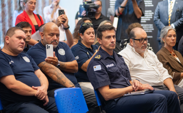 Policías sentados, observan a las autoridades firmando un documento 
