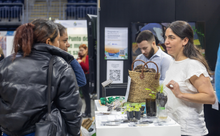 Más de 20.000 personas participaron en la Expo Uruguay Sostenible Dos mujeres hablan con otra que se ubica detrás de una mesa pequeña, en la que hay plantas ubicadas en envases de plástico