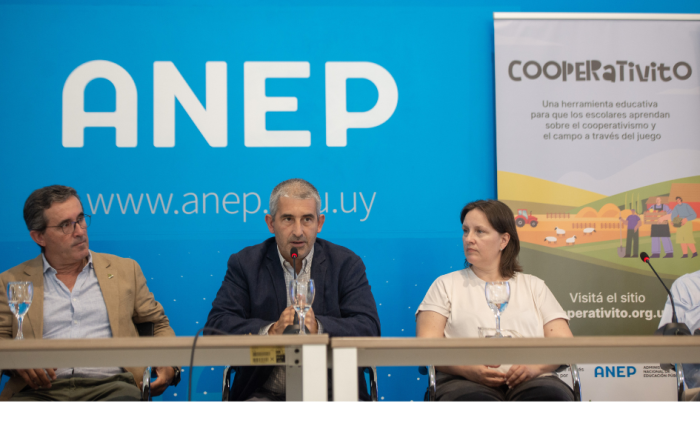En 2026 reabrieron 10 escuelas rurales en distintas localidades Presidente de ANEP, Pablo Caggiani, brinda un discurso sentado. A su lado, la directora de Primaria, Gabriela Salsamendi. Detrás un back con el logo de ANEP y un banner con la leyenda "Cooperativito"