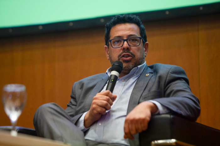 Secretario de la Presidencia, Alejando Sánchez, sentado en un sillón con la pierna cruzada, habla con micrófono en mano