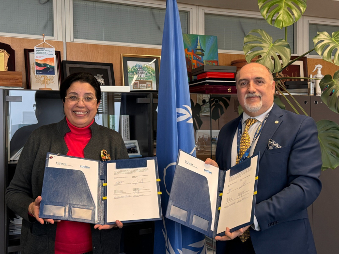 El embajador de Uruguay en Austria, Alejandro Garofali, y la directora general adjunta y jefa del Departamento de Ciencias y Aplicaciones Nucleares de OIEA, Najat Mokhtar, sostienen una carpeta con un documento firmado.