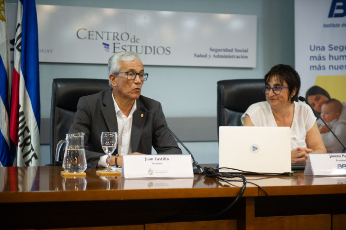 Ministro de Trabajo, sentado, habla al público. A su lado, la presidenta del BPS, Jimena Pardo, lo observa atentamente