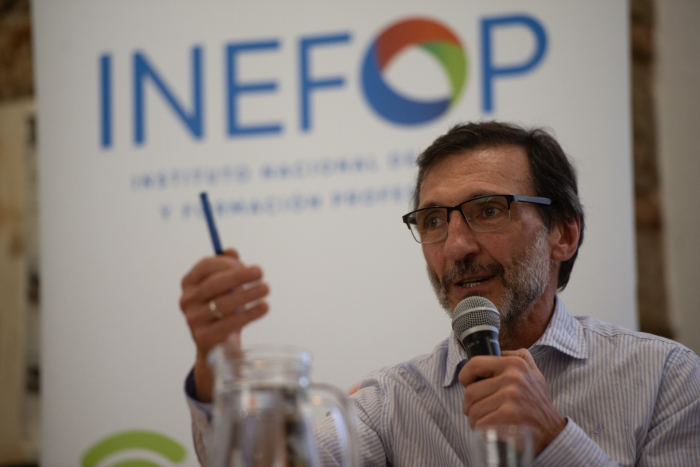Director de Inefop, Miguel Venturiello, habla con micrófono en mano. Con su otra mano, sostiene una lapicera. En el fondo, un banner con el logo de Inefop