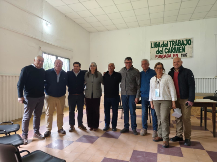 Ministra de Transporte y Obras Públicas, Lucía Etcheverry, de pie, junto a integrantes de la Liga de Trabajo del Carmen. En el fondo, un cartel con la leyenda "Liga de Trabajo del Carmen. Fundada en 1907"