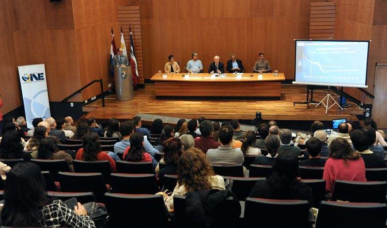 Vista desde atrás de la sala del evento con la mesa de autoridades y el público