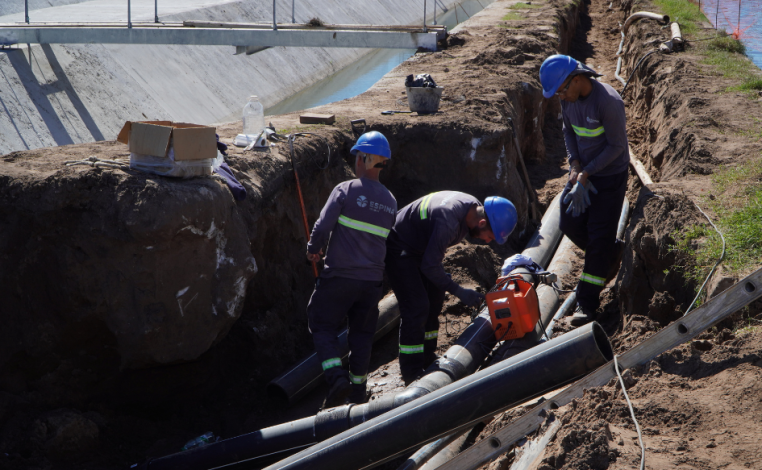 Tres obreros manipulan tuberías en una zona excavada
