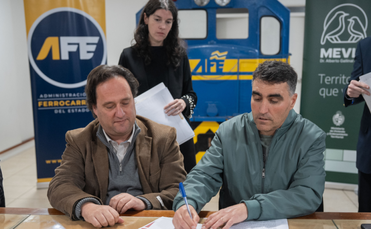 Presidentes de Mevir y AFE, Andrés Lima y Ernesto Cesar, firman un acuerdo de cooperación. Detrás de ellos, una funciona