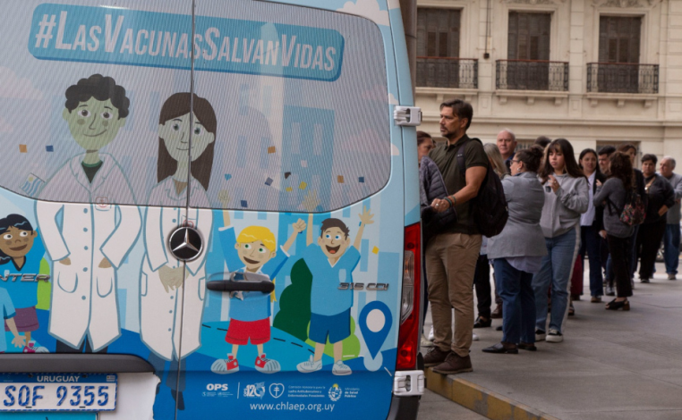 Decenas de personas, en fila, aguardan para ingresar a un vacunatorio móvil ploteado con la leyenda "Las vacunas salvan 
