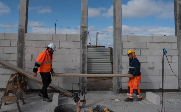 Dos obreros trasladan una tabla, cada uno desde una punta, en el predio donde se construye la policlínica de Estación At