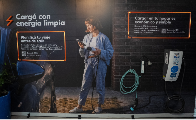 Imagen interior del stand de UTE en la Expo Prado 2026. Una mujer joven sostiene un cargador de autos eléctricos. Se lee