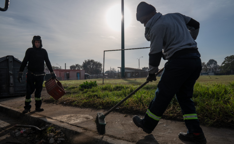 Dos funcionarios que trabajan para la Intendencia de Montevideo barren una vereda en Cerro Norte