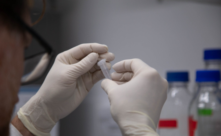 Científico manipula un tubo de ensayo entre sus manos con guantes