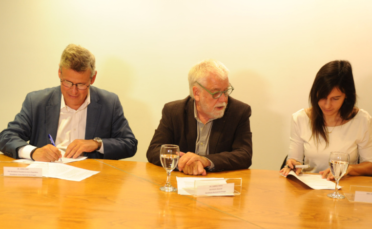 Prosecretario de Presidencia, Jorge Díaz, y rectora de UTEC, Valeria Laurnadie, firman un convenio. En el medio, los obs