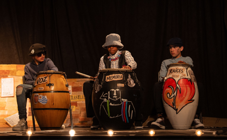 Tres escolares tocan un tambor en el escenario, durante la primera edición de La Escuela en Escena