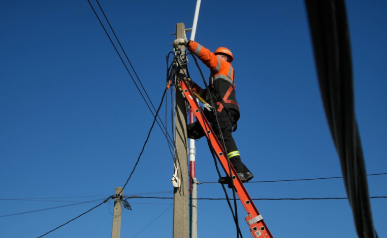 Funcionario de UTE subido a una escalera manipula el cableado en la vía pública