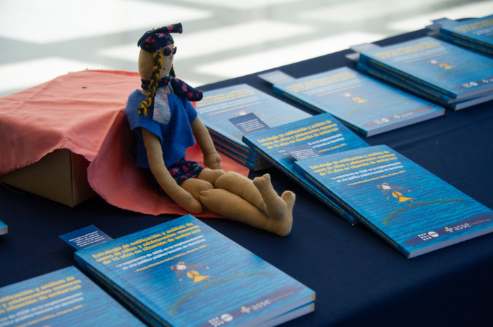 Muñeca sentada en una mesa, rodeada de ejemplares de libros