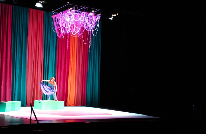 Mujer actúa en el escenario de un teatro. Detrás, un telón de colores