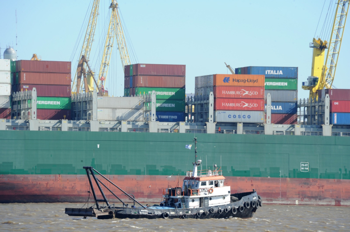 Buque portacontenedores arriba a puerto de Montevideo. Delante de él, un barco remolcador.