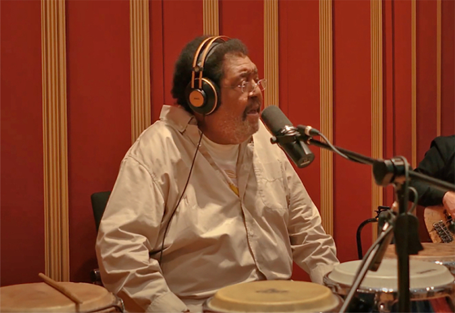 Rubén Rada canta frente a un micrófono, con auriculares y tambores, durante una sesión de grabación.