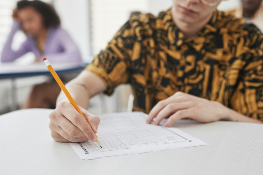 Estudiante completa con lápiz una prueba escrita en un salón de clase.
