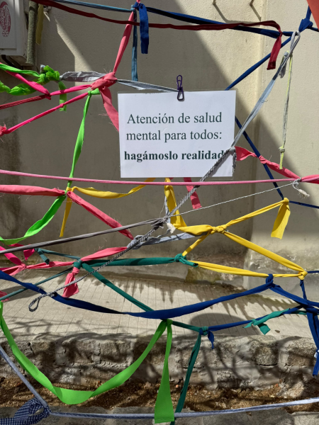 Cartel reclama atención de salud mental para todos, rodeado de cintas de colores.