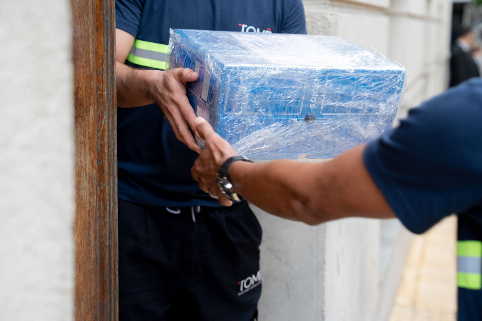 Personal de traslado manipula cajas de documentación histórica. Dos operarios trasladan una caja azul envuelta en plástico junto a una puerta.