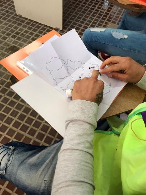 Taller en Unidad de Rehabilitación N°13 de las Rosas. Manos de participante con carpeta y trabajos.