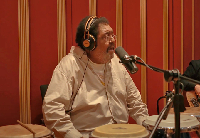 Rubén Rada canta frente a un micrófono, con auriculares y tambores, durante una sesión de grabación.