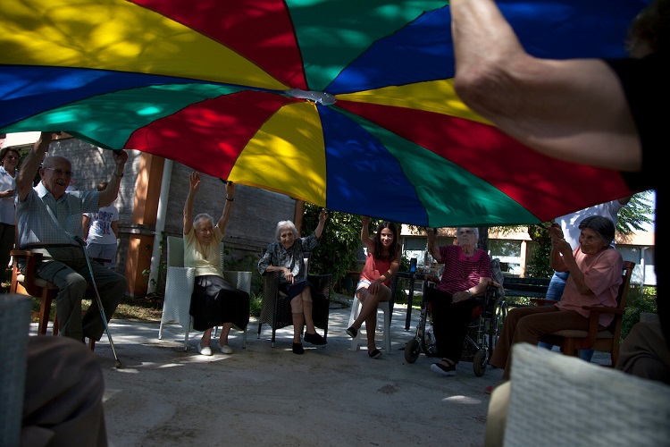 Hogar de Colonia Miguelete. Personas mayores sentadas en ronda jugando con una tela grande y colorida.