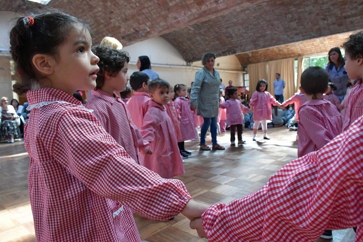 Niños y niñas de delantal a cuadrados hacen ronda en el jardín de infantes