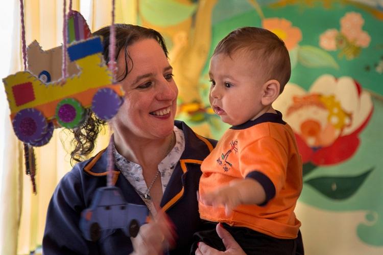 Educadora con niño pequeño en brazos, en jardín en Florida