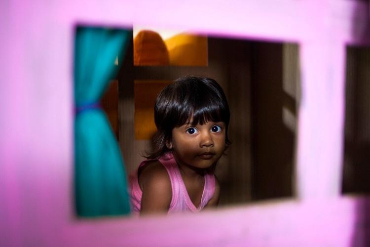 Niña pequeña mira por la ventana de una caja de juguete en Casa Comunitaria de Cuidados