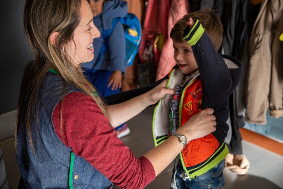 Facilitador de Autonomía Ambitos Educativos llamado información concurso postularse Maestra ayudando a un niño a ponerse la campera en un centro educativo
